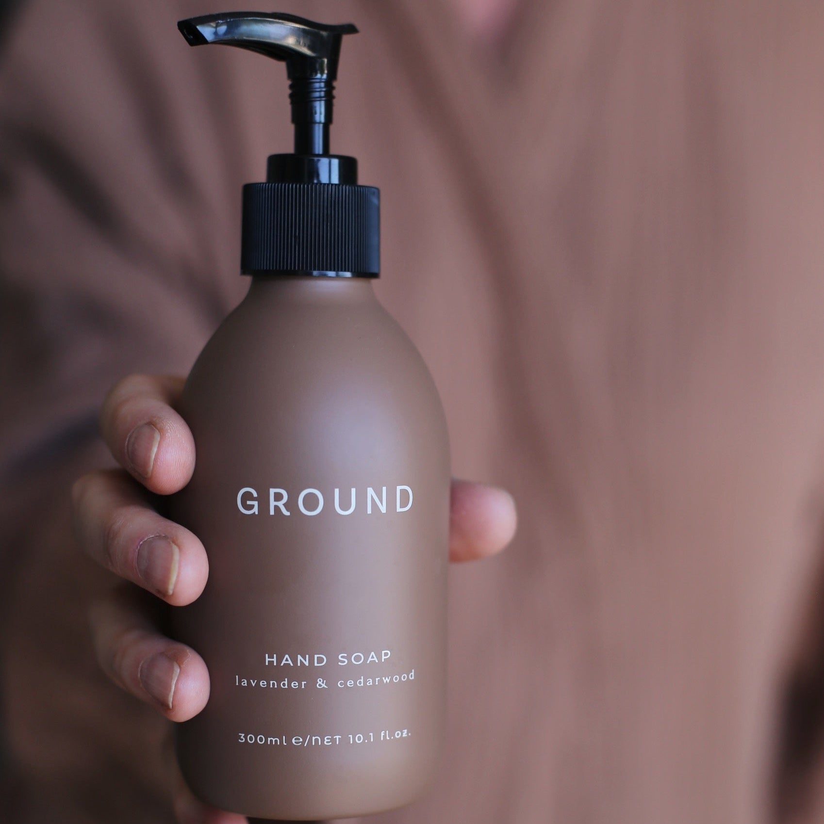 Hand holding a 'GROUND' hand soap bottle against a blurred background