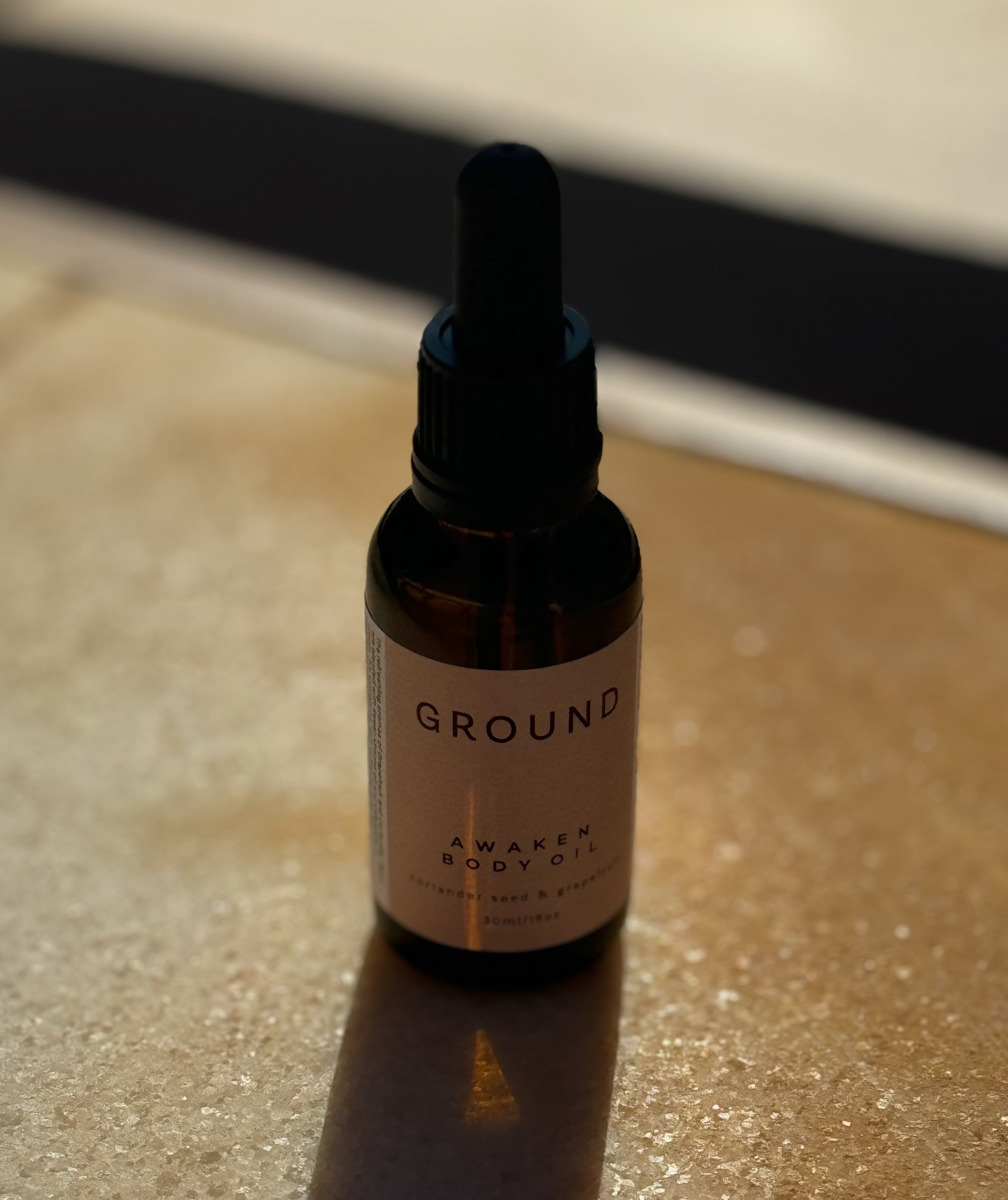 Image of brown glass bottle 30ml in size with a black dropper lid. It has a neutral beige label describing the contents as Awaken Body Oil.