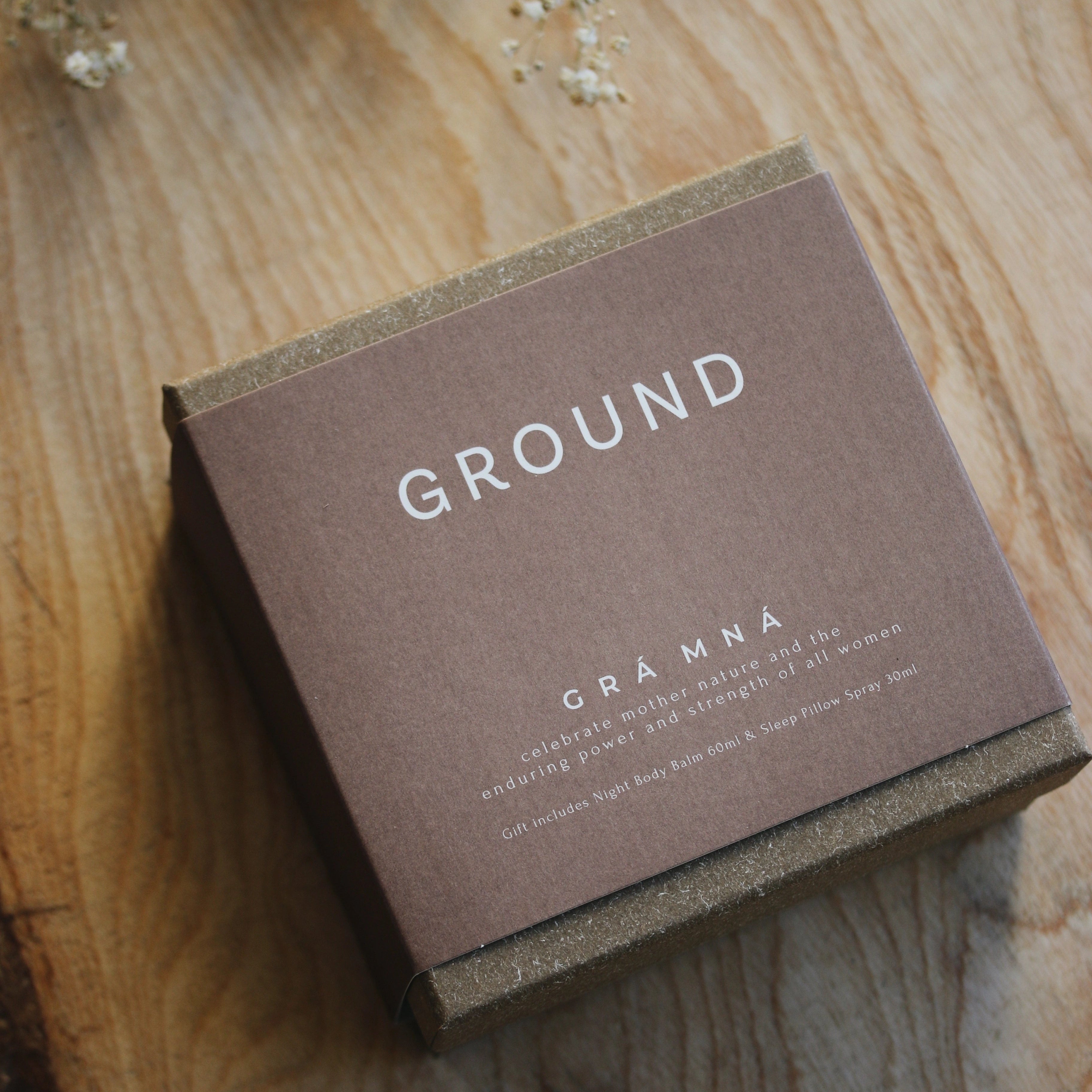 Photo of the outside of GROUND Gra Mna gift box. It is a square cardboard box with a neutral brown sleeve. It tell us that the Gra Mna gift set is ideal to celebrate mother nature and the enduring power and strength of all women. Gif includes Night Body Balm 60ml and Sleep Pillow Spray 30ml.