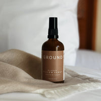 Ground Sleep Pillow Spray in a 100ml brown glass bottle. Sitting on a beige scarf. Contains rosewood and lavender.