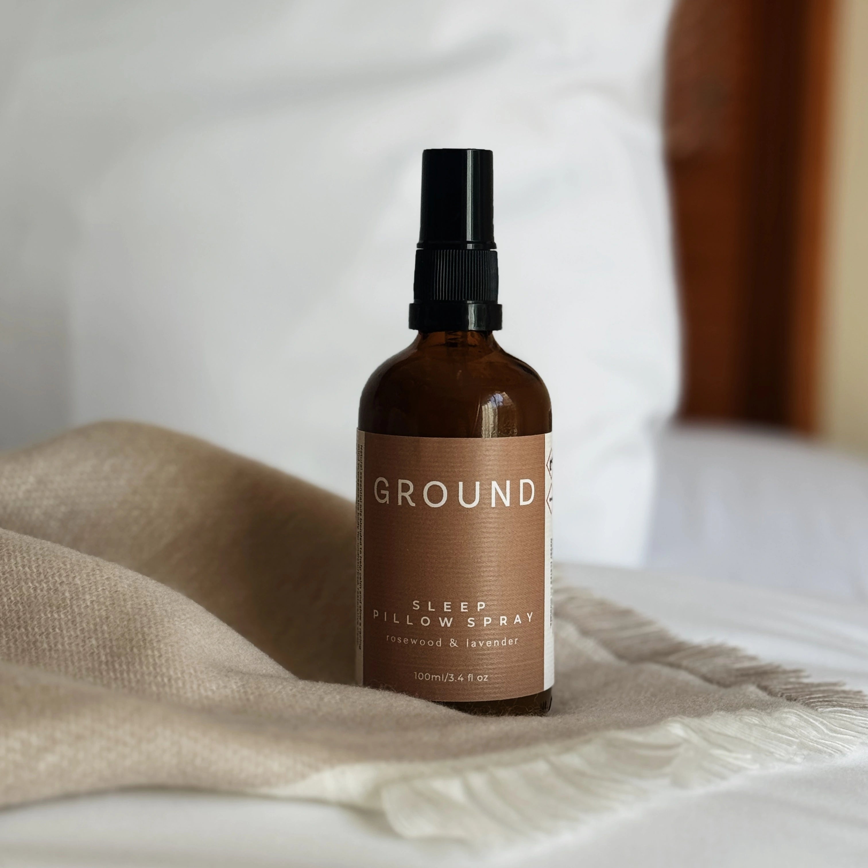 Ground Sleep Pillow Spray in a 100ml brown glass bottle. Sitting on a beige scarf. Contains rosewood and lavender.