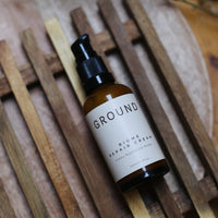 Image of a brown glass bottle with pump dispenser lying flat on a wooden rack on top of a wooden surface. It is a 50ml bottle.