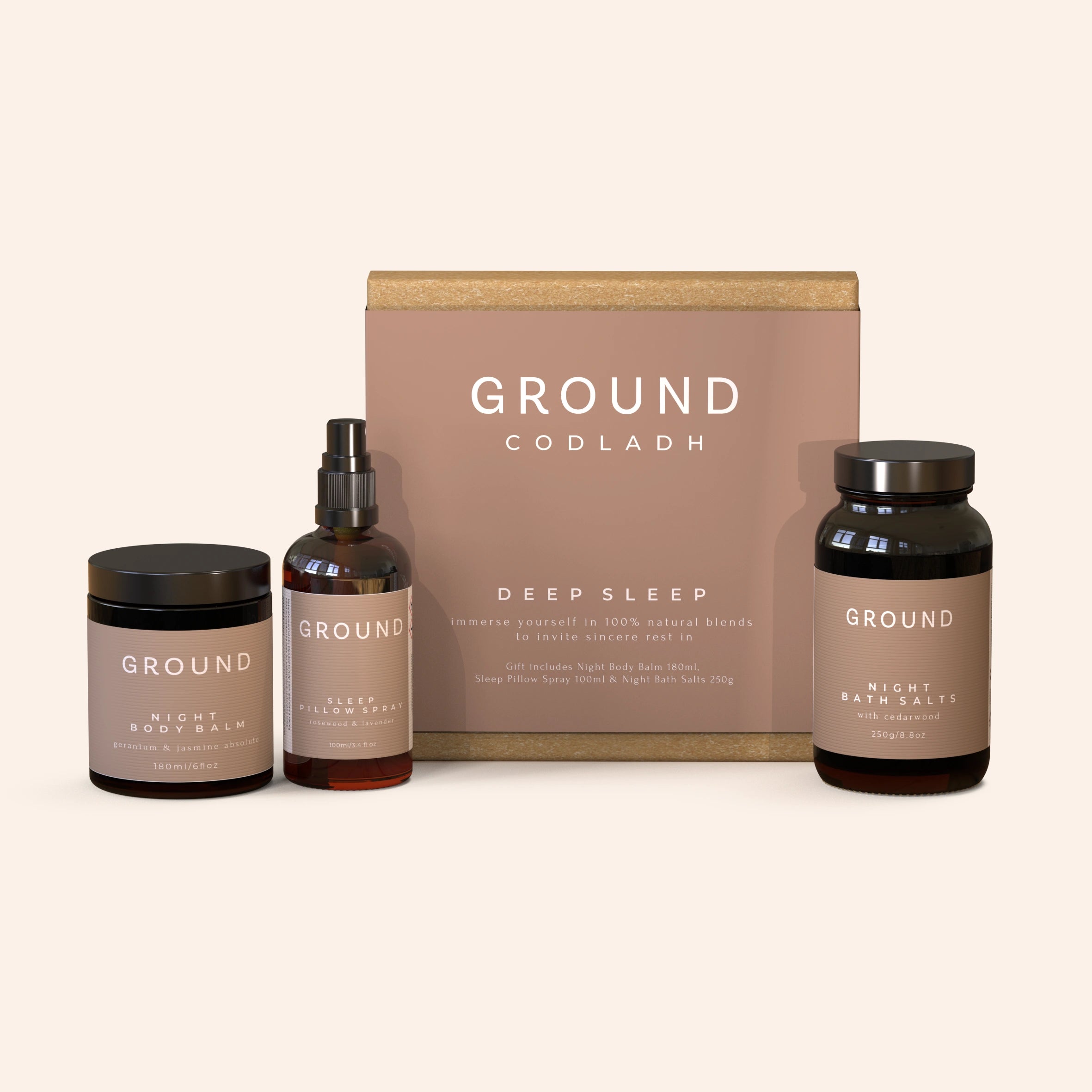 A gift set from Ground Codladh including a bottle of Night Sleep Body Balm, a jar of Night Bath Salts, and a spray bottle labelled Sleep Pillow Spray, all presented in front of a brown cardboard box with the brand name 'GROUND' printed on it.
