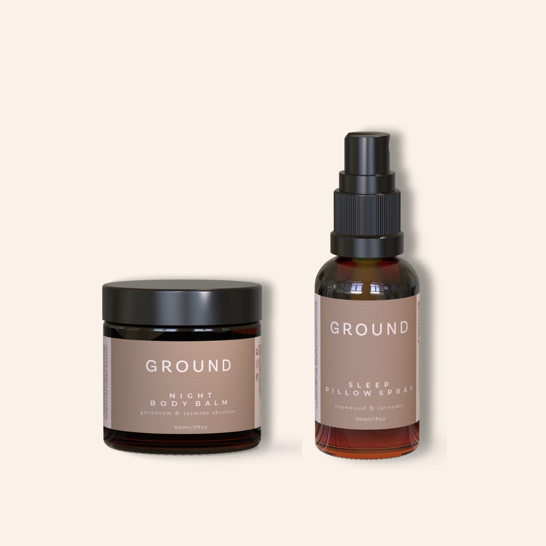 Two 'GROUND' products on a beige background. The Night Body Balm is presented in a brown glass jar and sits beside a brown glass spray bottle of sleep pillow spray containing lavender.