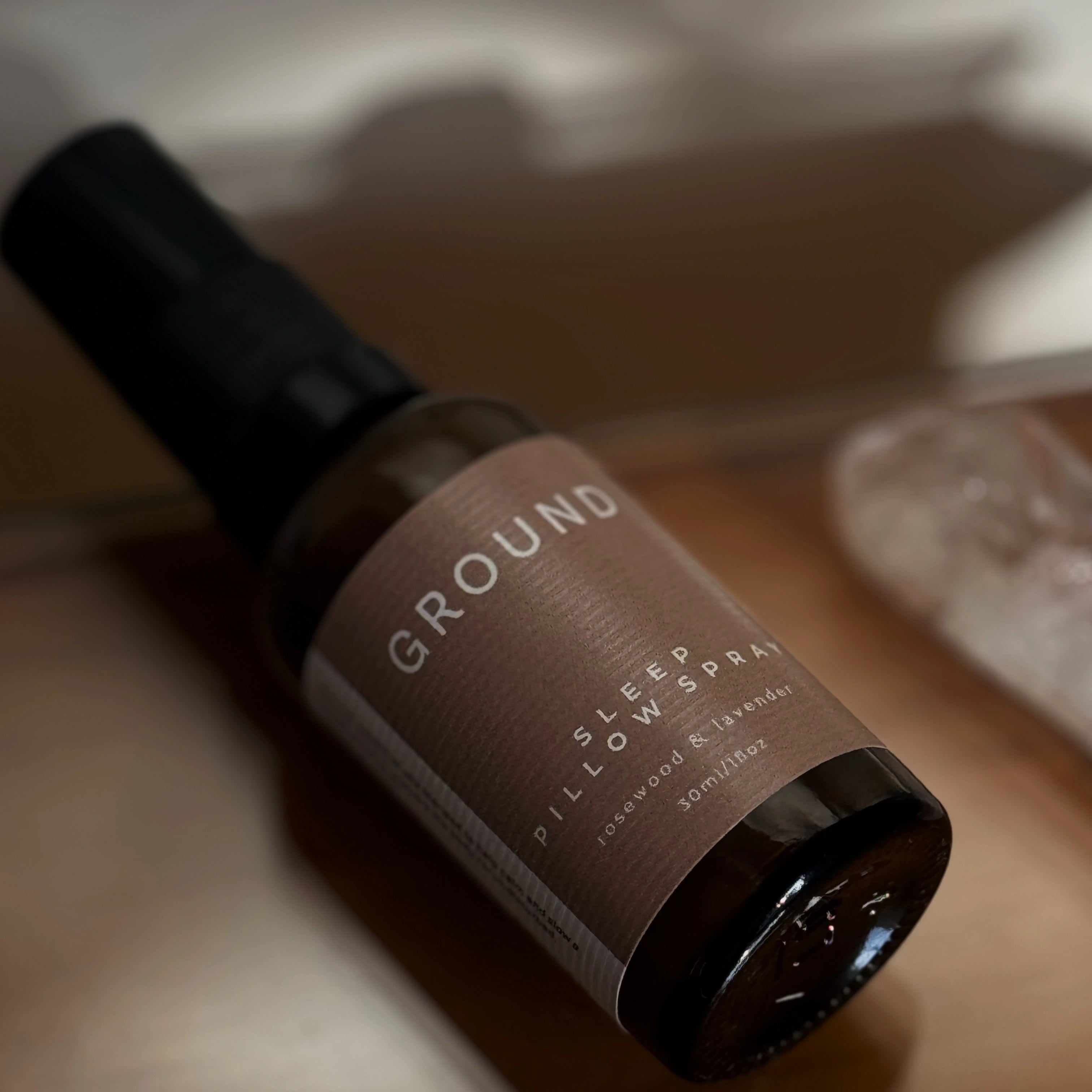 Image of a brown glass bottle on its side with a neutral brown label reading GROUND Sleep Pillow Spray Rosewood & Lavender 30ml / 1 fl oz.