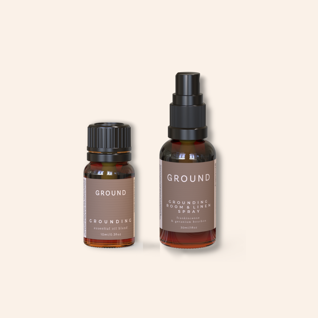 Two bottles of 'GROUND' products on a beige background. One is Grounding Essential Oil Blend 10ml and the other Grounding Room and Linen Spray 30mls. Both are presented in brown glass bottle with brown label with cream writing.