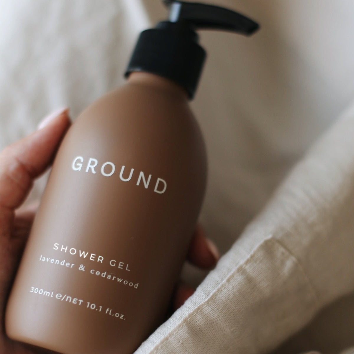 A brown bottle of Ground shower gel in a hand