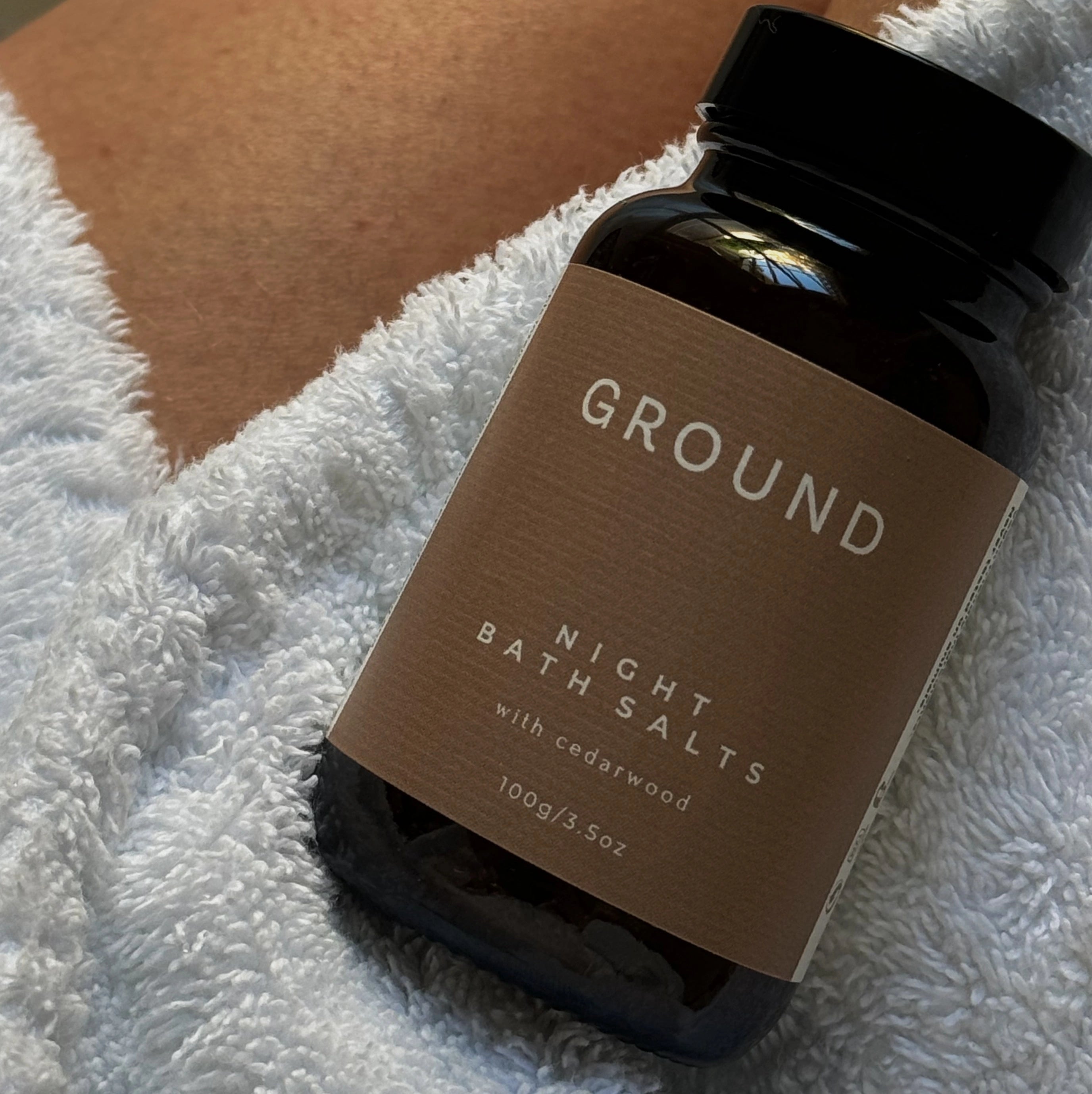 Jar of Ground night bath salts with cedarwood sitting on a white towel. 100g in weight.