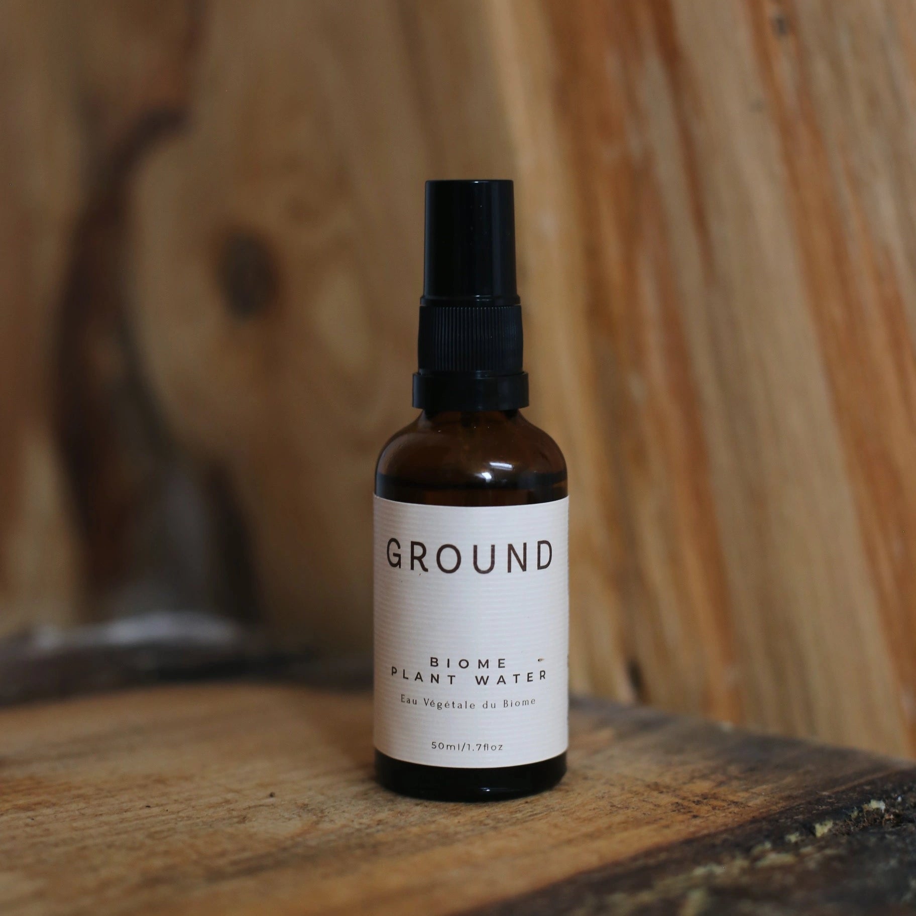 Image of a bottle of Ground Biome Plant Water sitting on fresh tree trunk plank.
