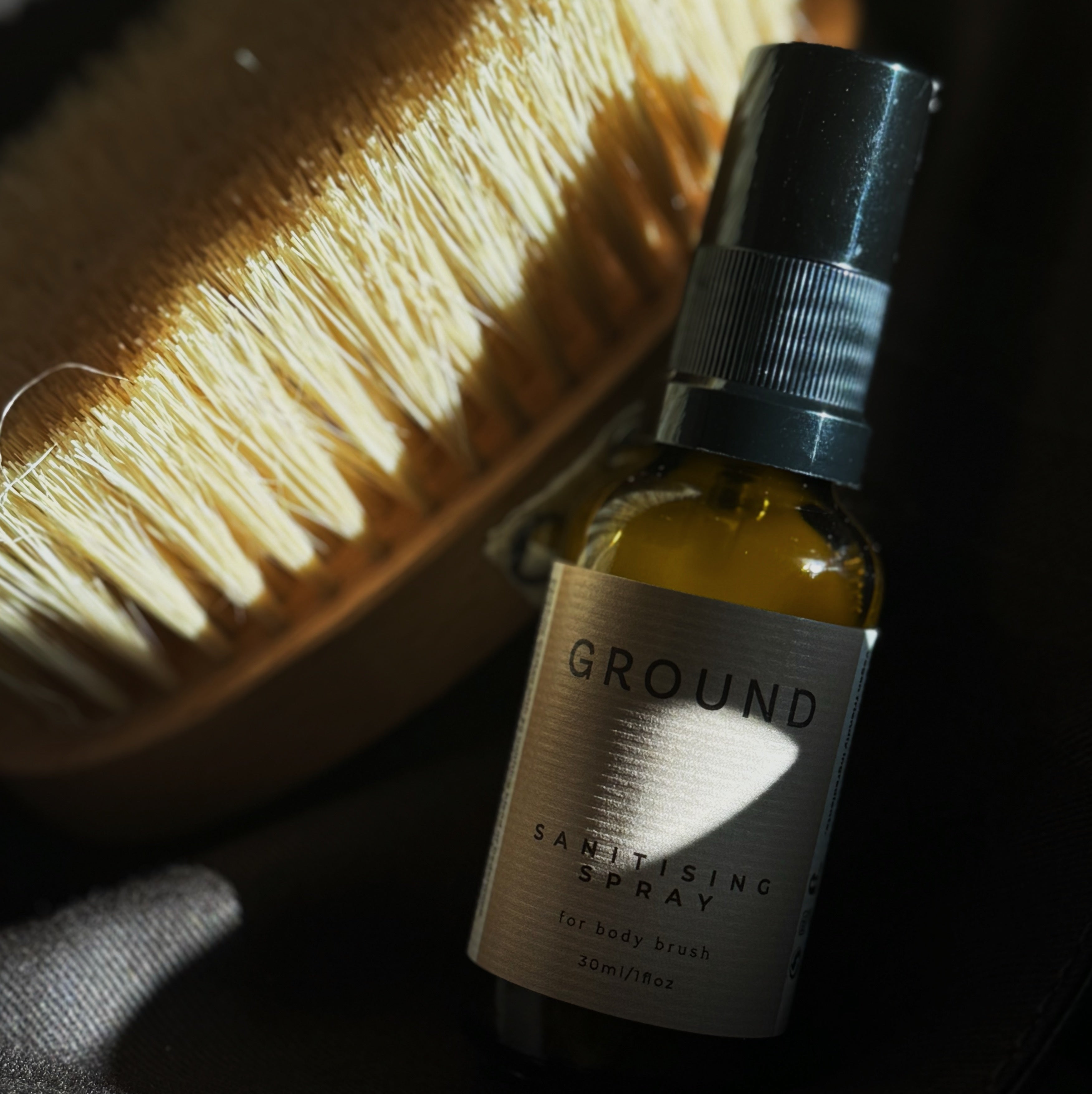Photo of a bottle of 30ml sanitising spray for body brush sitting adjacent to a body brush in the sunlight.