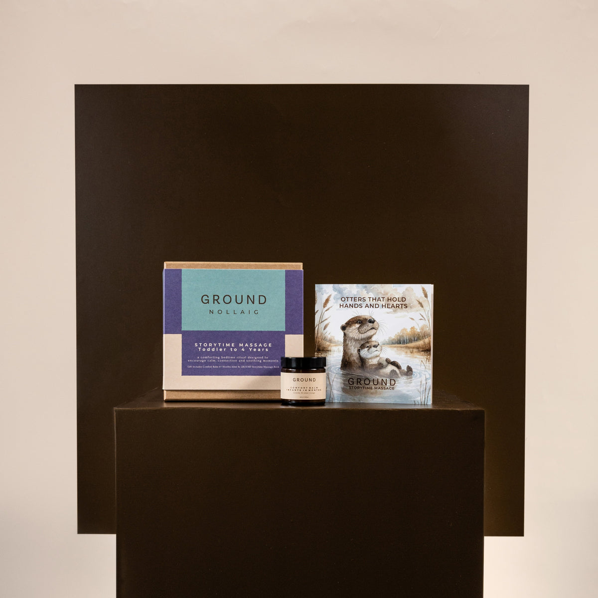 A gift box with comfort balm and childrrens book on a dark pedestal against a beige wall. 
